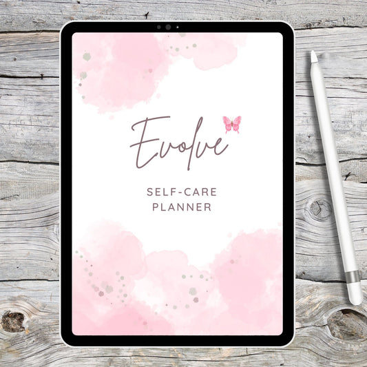 Black tablet laying on grey and white wooden desk with a white stylus pen by the right of the tablet.  Tablet displaying pink and white self-care digital planner cover page.