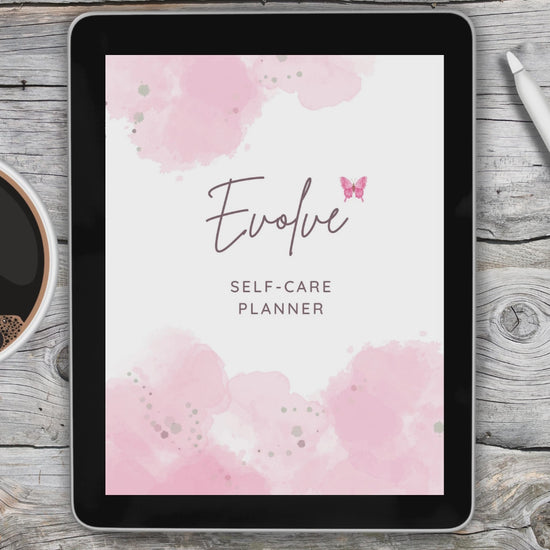 Black tablet laying on grey and white wooden desk with a white stylus pen on the right of the tablet and a cup of coffee on the left of the tablet.  Tablet displays video of self care digital planner.