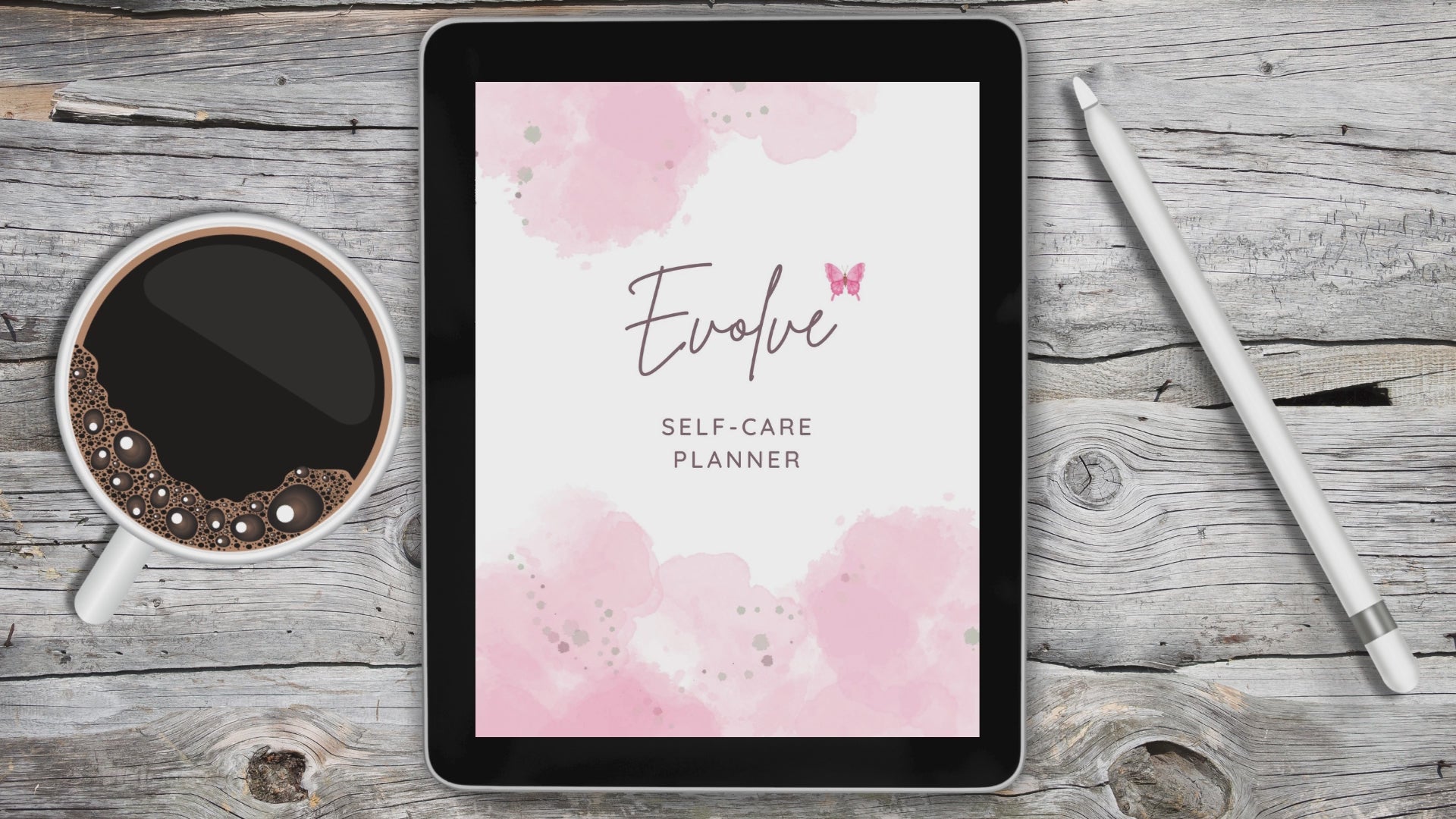 Black tablet laying on grey and white wooden desk with a white stylus pen on the right of the tablet and a cup of coffee on the left of the tablet.  Tablet displays video of self care digital planner.